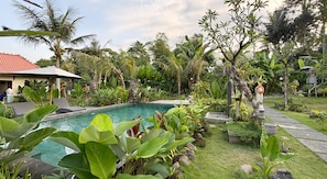 A pool surrounded by lush greenery, a pathway, and a building with a red roof. - Laksmi Viridis Villas (Gianyar)