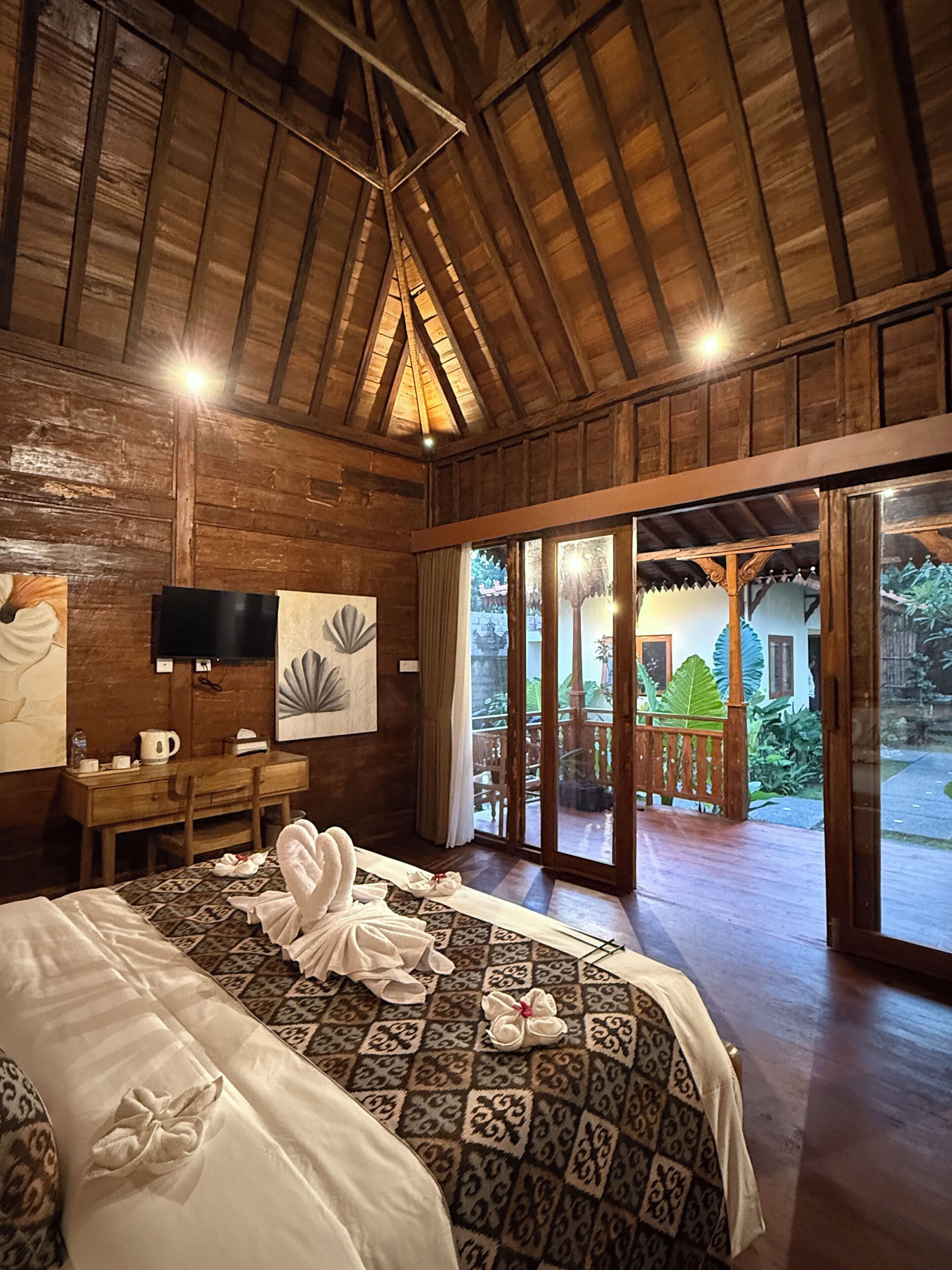 A wooden room with a bed, a desk, a TV, and a view of an outdoor area.