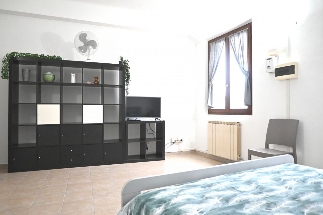 A bedroom with a bed, a TV, a radiator, a fan, and a window with curtains.