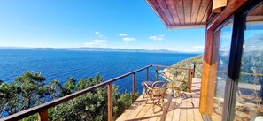 A wooden deck with a view of the sea, a glass door, and two wicker chairs. - La Caouanne Lodges: Panoramic sea view at the Île du Levant naturist resort (Hyères)