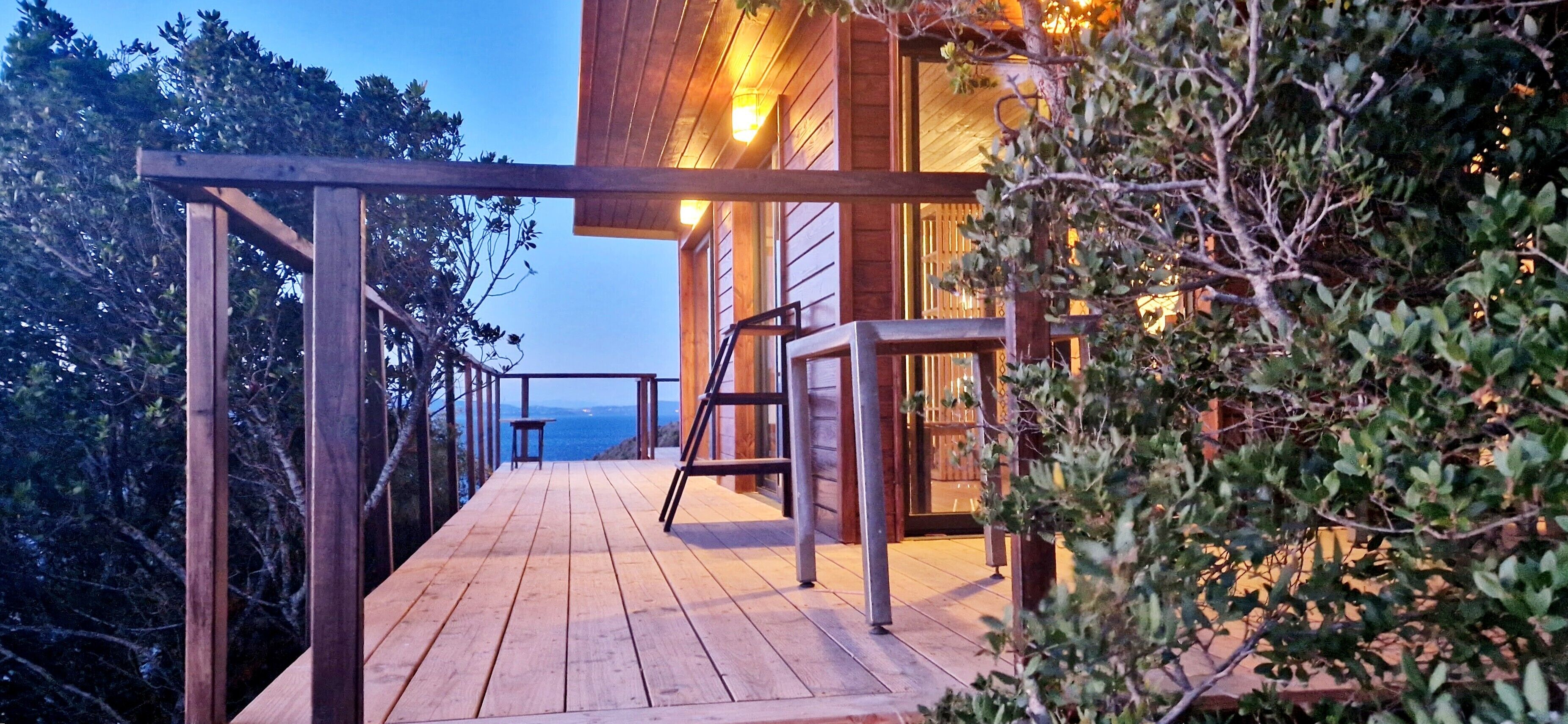 Een houten terras met uitzicht op zee, een houten balustrade en een tafel.