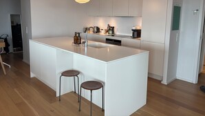 Una cocina moderna con una isla central, taburetes de bar, una lámpara colgante y un horno empotrado.