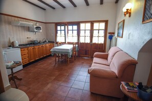 A kitchen with wooden cabinets, a dining table with chairs, a pink sofa, and a radiator. - Casa Victor - Apartment 3 (La Orotava)