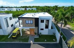 A modern two-story house with a flat roof, a wooden door, and a small front yard. - Lux 2-Story 3BR Villa + Private Pool (Punta Cana)