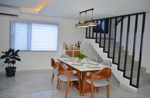 A dining area with a long table, chairs, a potted plant, and a staircase with black railings. - Lux 2-Story 3BR Villa + Private Pool (Punta Cana)