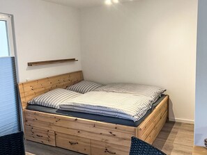Ein Einzelbett mit Holz-Kopfteil, Schubladen, einem Nachttisch und einem Regal darüber.