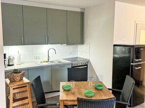 Eine kleine Küche mit grauen Schränken, einer Spüle, einem Herd und einem schwarzen Kühlschrank.