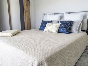 Ein ordentlich bezogenes Bett mit einer gesteppten Tagesdecke, einer zusammengelegten Decke und einem Kopfteil mit mehreren Kissen.