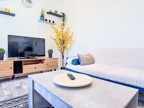 Un saló modern amb televisió de pantalla plana, una taula de centre amb un comandament a distància, un sofà amb coixins i plantes decoratives sobre els prestatges.