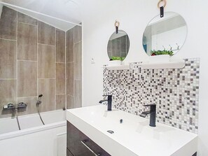 Ein Badezimmer mit einer Badewanne, zwei Waschbecken, einem Spiegel und einer gefliesten Rückwand.