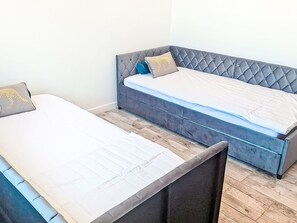 Two single beds with grey headboards and white bedding, a wooden floor, and a plain wall. - Impasse des cabanons by Interhome (Cadolive)