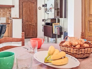 A dining area with a table set for breakfast, including a plate of bananas, a basket of croissants, and a red mug. - Villa le Cédre 17 by Interhome (Six Fours)