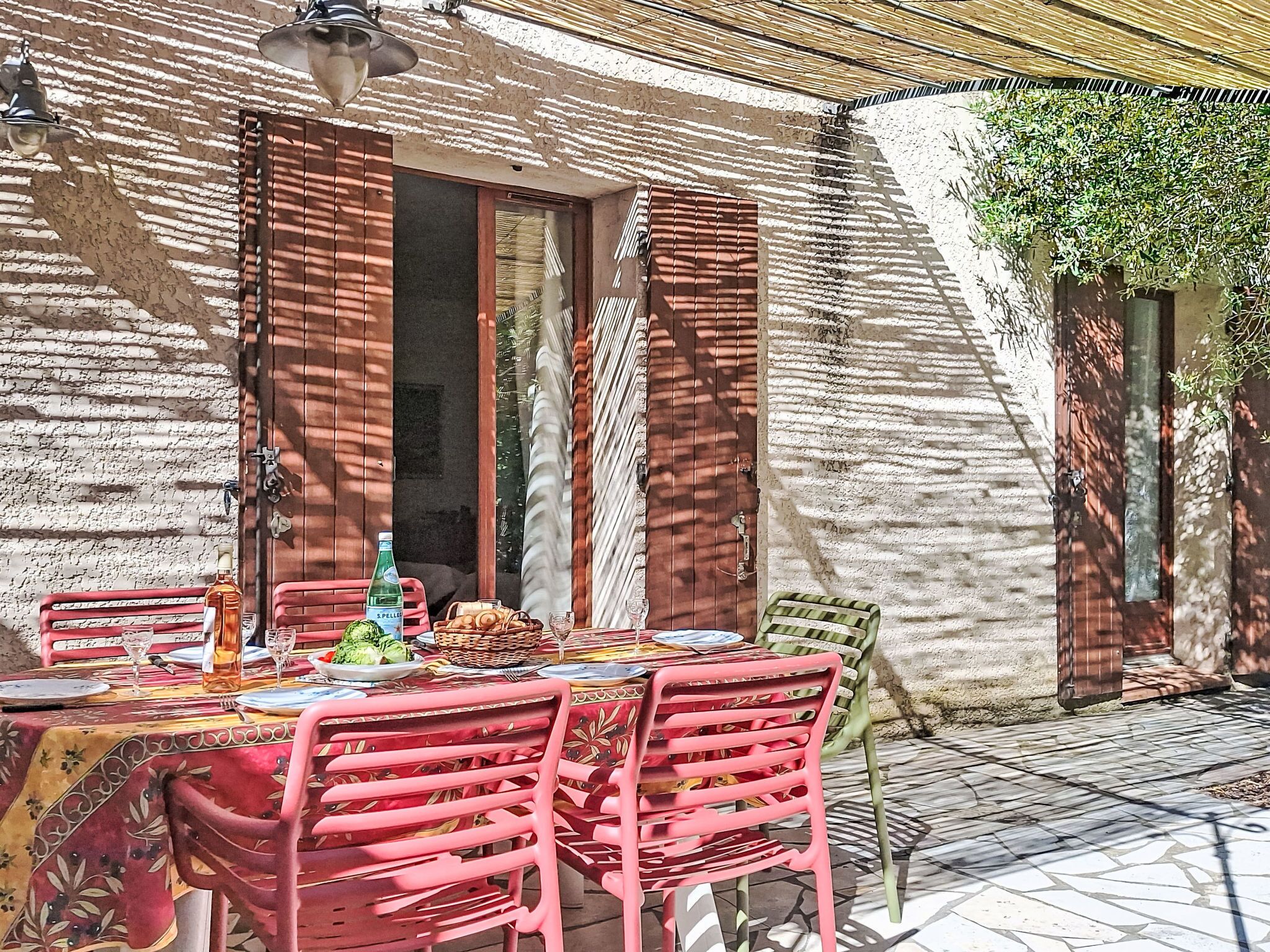 Un espace de restauration en plein air avec une table dressée pour deux personnes, entourée de chaises rouges, d’un panier en osier et d’une bouteille d’eau.