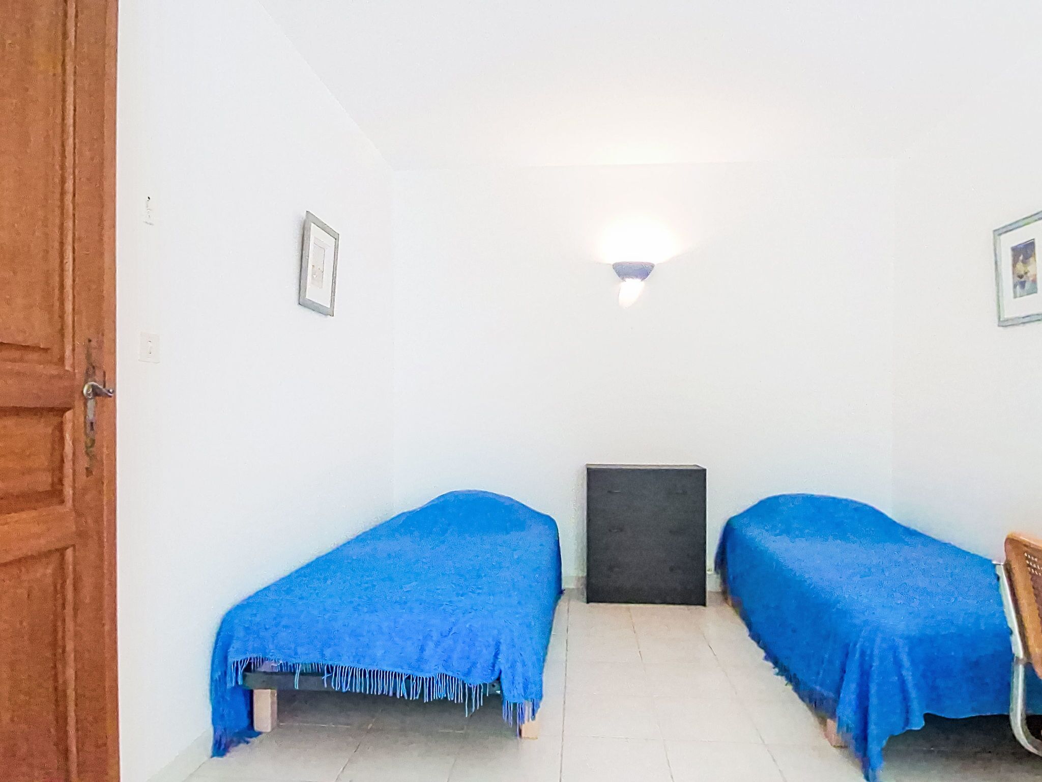 A small room with two beds, a door, a light fixture, and a wall-mounted air conditioning unit.
