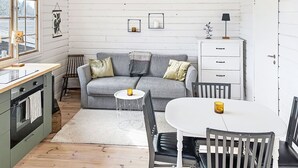 Ein gemütliches Interieur im Chalet-Stil mit einem grauen Sofa, einem weißen Esstisch und einer Küchenzeile.
