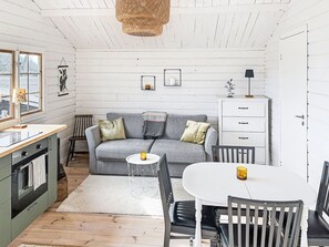 Ein gemütliches Interieur im Chalet-Stil mit einem grauen Sofa, einem weißen Esstisch und einer Küchenzeile.