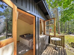 A wooden cabin with a bed, a small table, and a deck.
