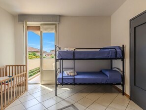 Ein Zimmer mit einem Etagenbett, einem kleinen Holz-Babybett und einer Tür zu einem Balkon.