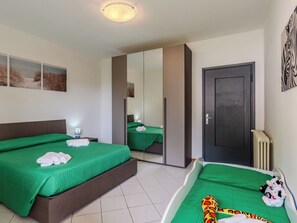 Quarto de hotel com duas camas, uma porta escura, radiador e obras de arte nas paredes.