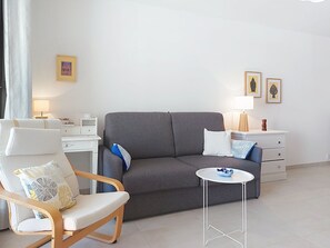 Een moderne woonkamer met een grijze bank, een witte fauteuil, een kleine ronde tafel en een witte dressoir met een lamp.