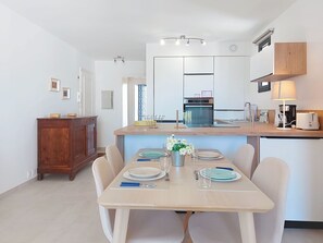 Een moderne keuken met een centraal eiland, een eethoek met een tafel gedekt voor twee personen, en een houten kast.