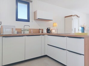 A modern kitchen with white cabinets, a built-in microwave, a coffee maker, and a window with blinds. - Le Luberon by Interhome (Six Fours La Coudoulière)