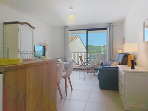 A living room with a dining area, a balcony with a view, and a TV on a wooden cabinet. - Le Luberon by Interhome (Six Fours La Coudoulière)