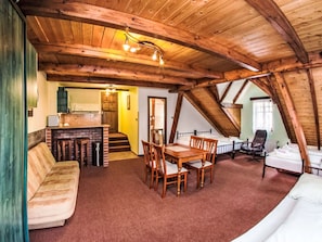 Ein gemütliches Dachzimmer mit Holzbalkendecke, einem Esstisch mit Stühlen, einer Couch und einem Bett.