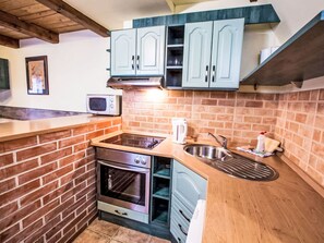 Eine kompakte Küche mit Backsteinrückwand, eingebautem Backofen, Mikrowelle und hellblauen Schränken.