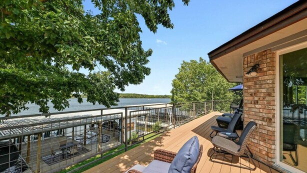 Een terras met buitenmeubilair, een glazen wand en uitzicht op een meer.