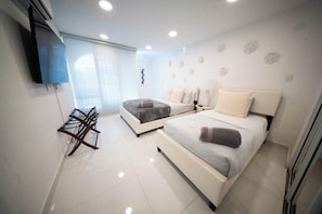 A modern bedroom with two beds, a TV mounted on the wall, and a drying rack. - Da Vinci Suites (San Juan)