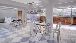 A spacious indoor area with a high ceiling, ceiling fans, and a view of a brick wall and greenery outside. - Palette Virar Mumbai (Vasai)