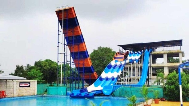 A swimming pool with two water slides, a building under construction, and a sign indicating a direction. - Palette Virar Mumbai (Vasai)