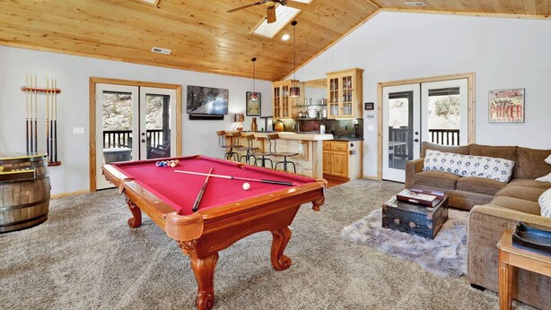 Une table de billard dans une pièce avec un plafond en bois, un coin cuisine et un espace salon avec un canapé et une table basse.