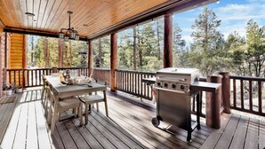 Une terrasse en bois avec une table et des chaises, un barbecue et une vue sur les arbres.