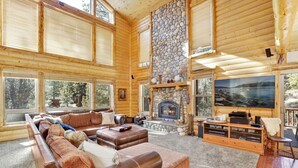 A log cabin interior with a stone fireplace, leather sofas, and a large TV. - Gold Rush Lodge, 6BR Hot Tub, GameRoom, Sleeps 16+ (Big Bear Lake)