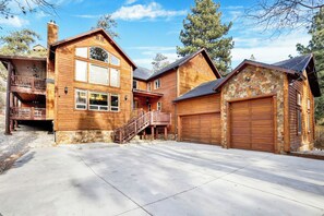 A large log cabin with a stone foundation, a covered porch, and a garage. - Gold Rush Lodge, 6BR Hot Tub, GameRoom, Sleeps 16+ (Big Bear Lake)