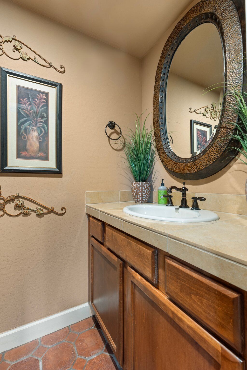 A bathroom with a vanity, a mirror, a sink, a potted plant, and a framed picture on the wall.