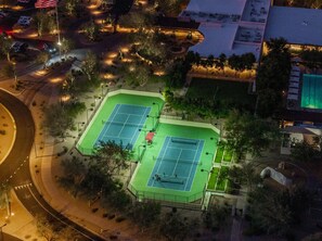 Luftaufnahme eines Tennisplatzkomplexes mit mehreren Plätzen, umgeben von Bäumen und einem Parkplatz.
