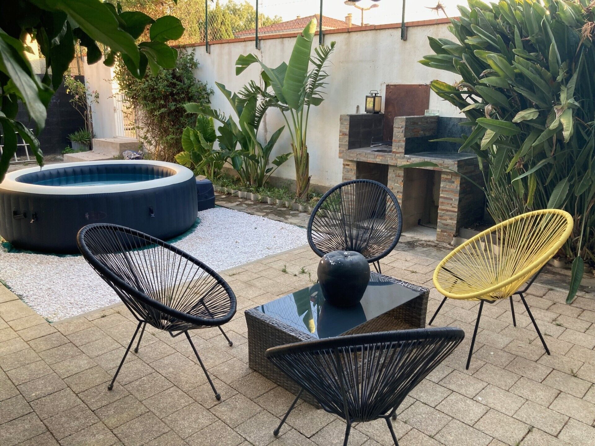 An outdoor patio with a hot tub, wicker chairs, and a barbecue area.