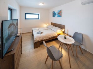 A bedroom with a bed, bedside table, chairs, a TV, a window, and a painting on the wall. - V Šachu by Interhome (Dačice)