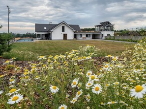 Ein modernes, zweistöckiges Haus mit flachem Dach, einer überdachten Terrasse und einem Swimmingpool im Hintergrund.