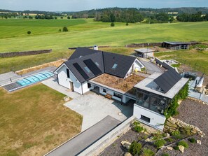 Une maison moderne dotée d’un grand patio, d’une piscine et offrant une vue sur la campagne environnante.