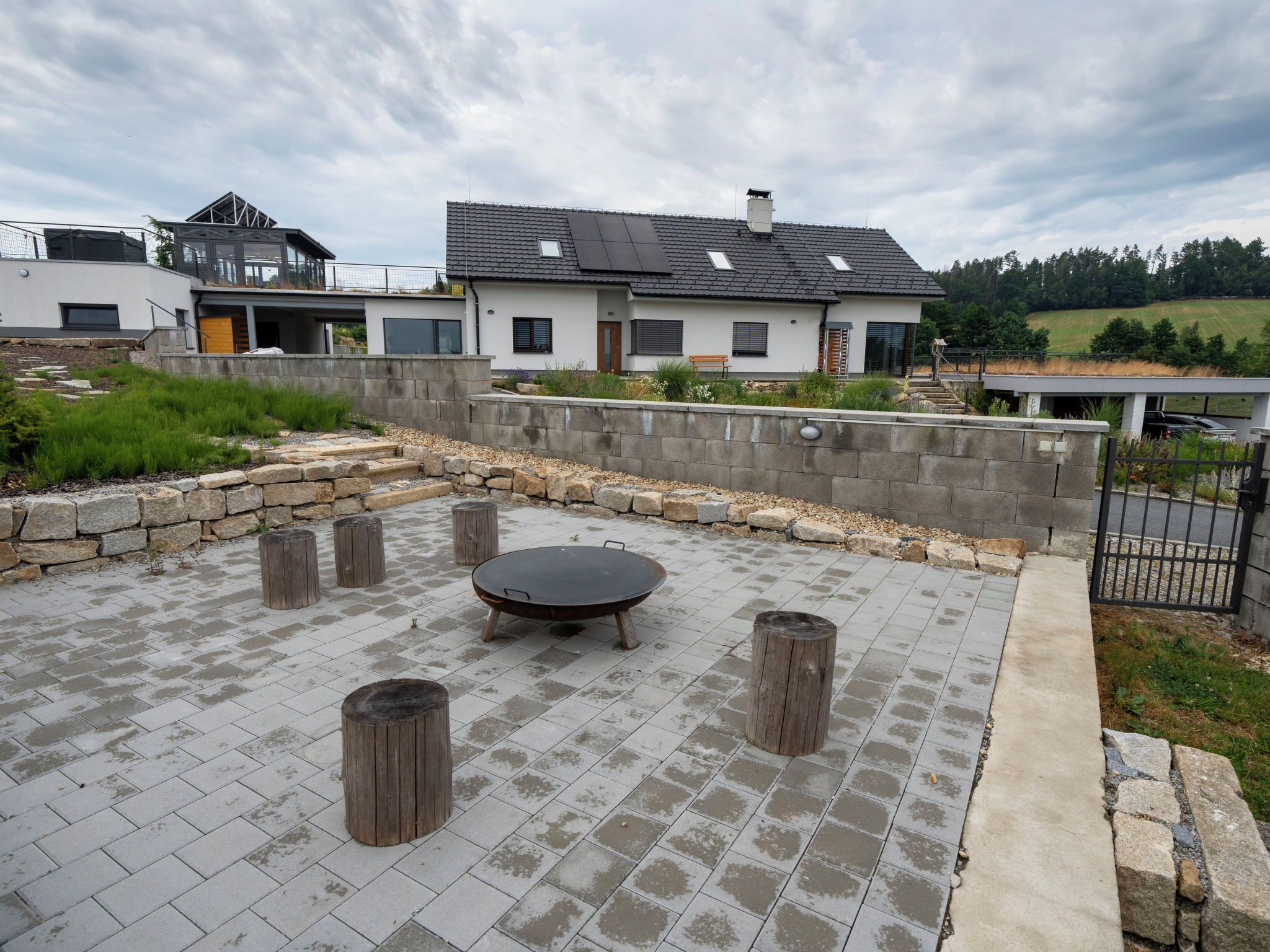 Un patio con una mesa redonda y taburetes, un muro de piedra y vistas a una casa moderna.