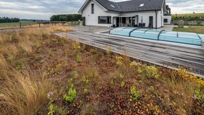 Et moderne hus med skråt tag, en overdækket terrasse og en have med træterrasse.