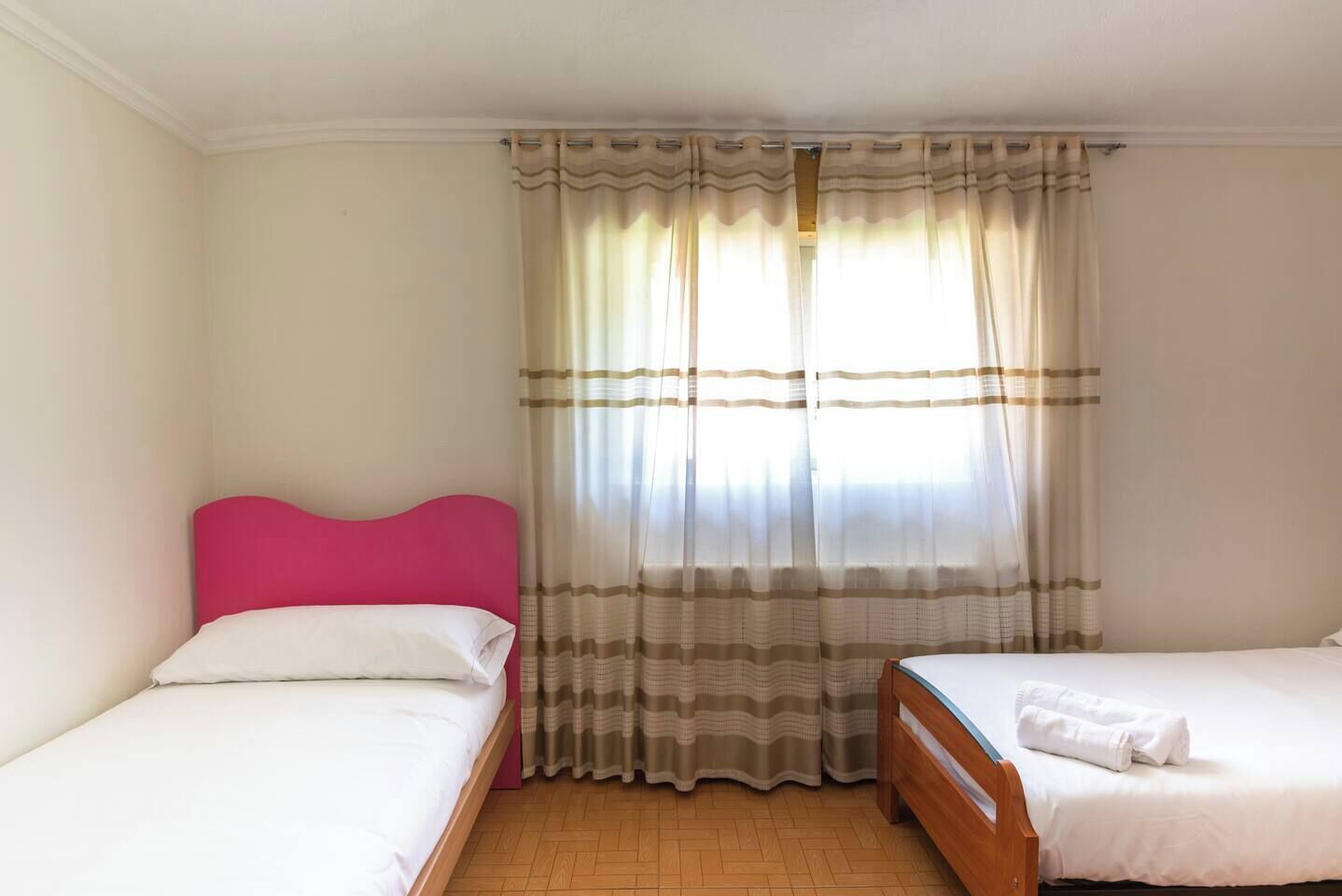 Habitació d'hotel amb dos llits, un sòl de fusta i una finestra amb cortines.