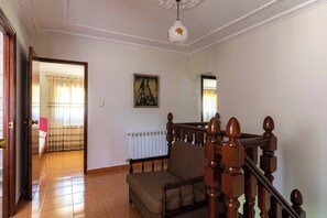 A staircase with a wooden handrail and balusters, leading to a room with a bed and a window with curtains. - Casa Pesquera - by Wehomes (Pesquera)