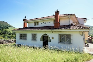 A two-story building with a tiled roof, a chimney, barred windows, and an open doorway.