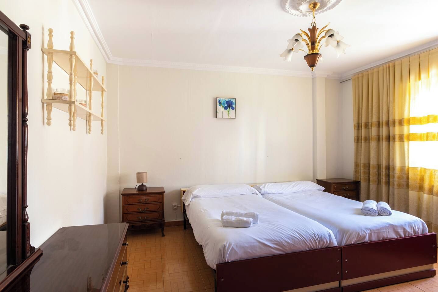 Habitación de hotel con una cama doble, una mesita de noche, una lámpara, un cuadro en la pared y una ventana con cortinas.