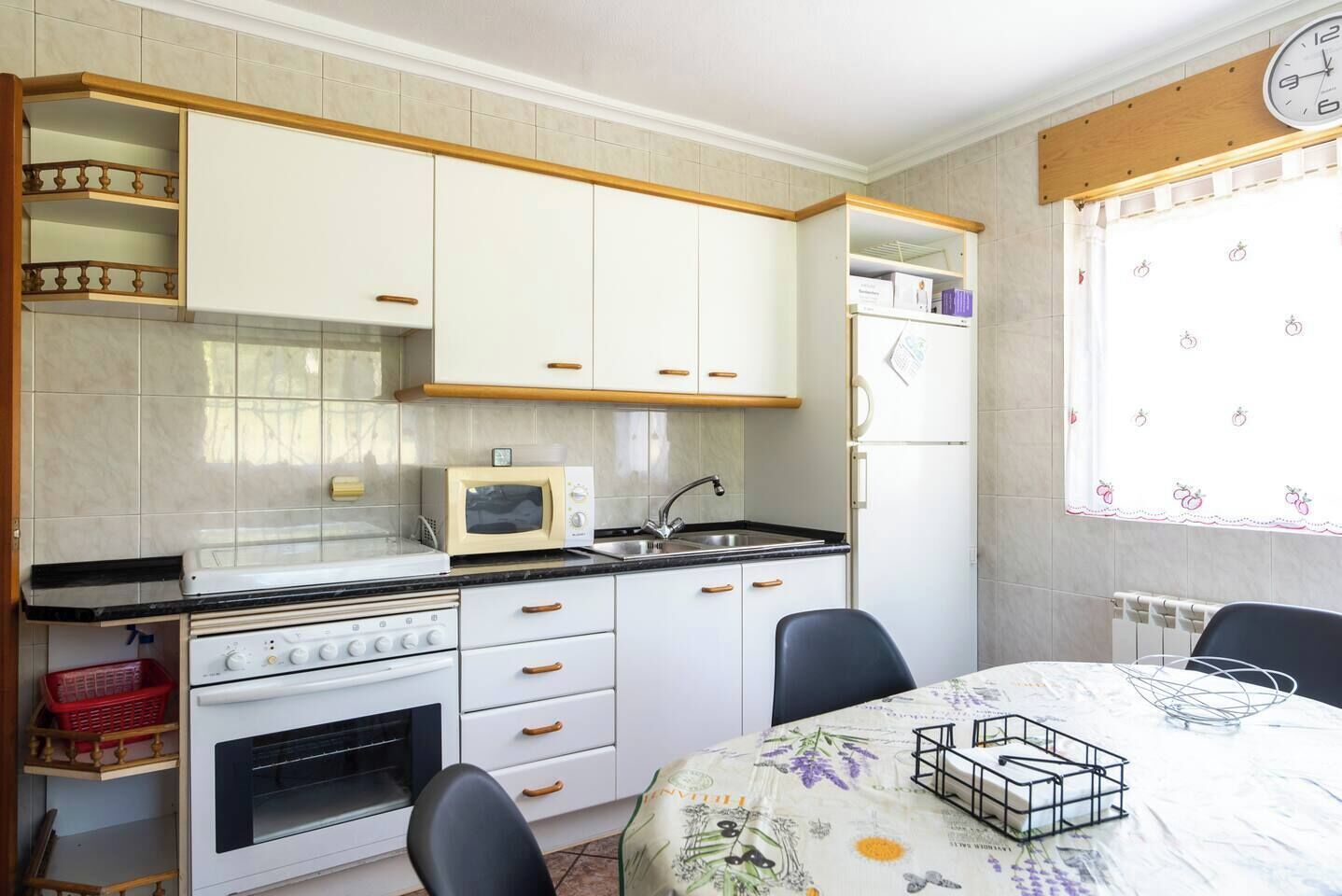 Una cocina compacta con armarios blancos, microondas, estufa y una mesa de comedor con sillas.
